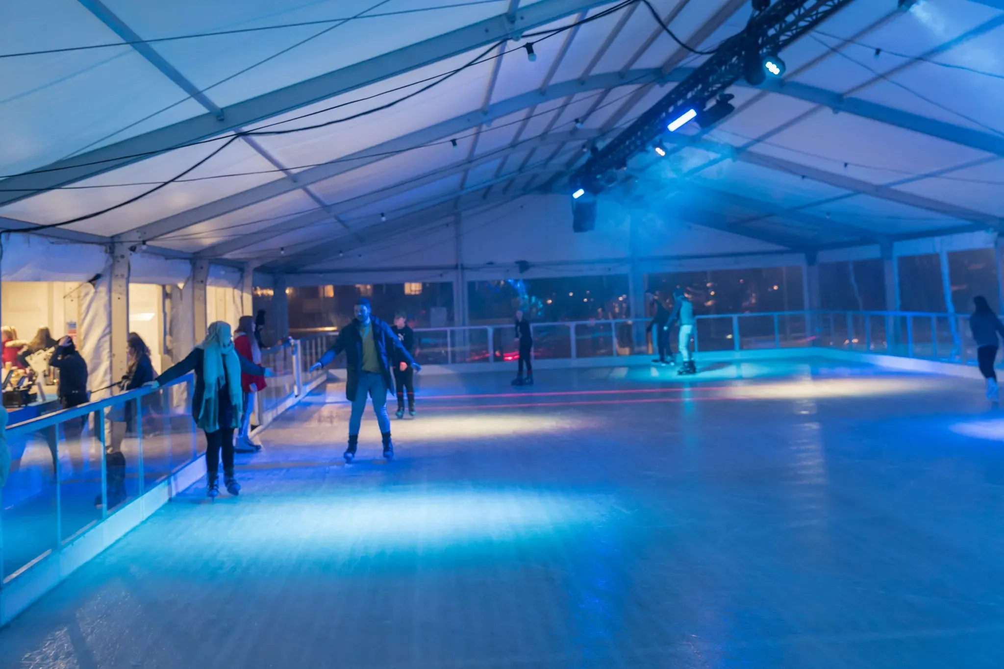 Skaters across the covered rink in Corby town centre under blue lighting