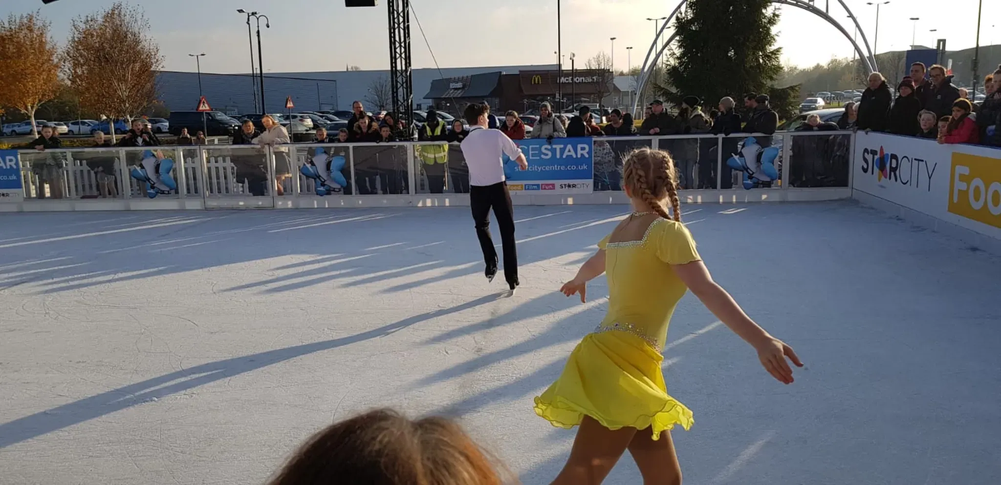 A figure skater in a yellow dress performing on the StarCity outdoor rink